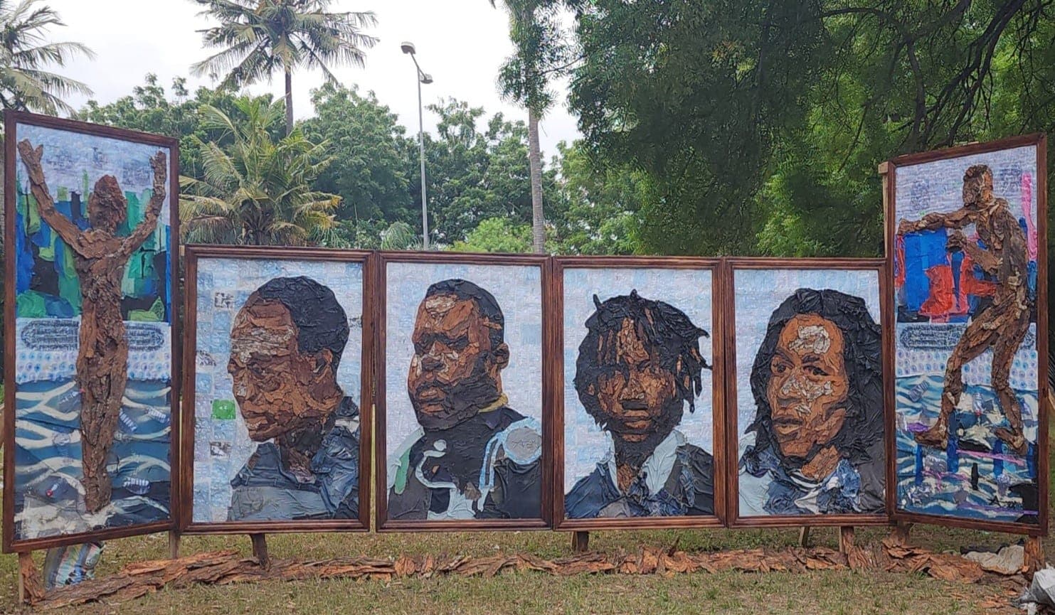 Six framed Nipadua bark-relief portraits installed outdoors, leaning together in a row