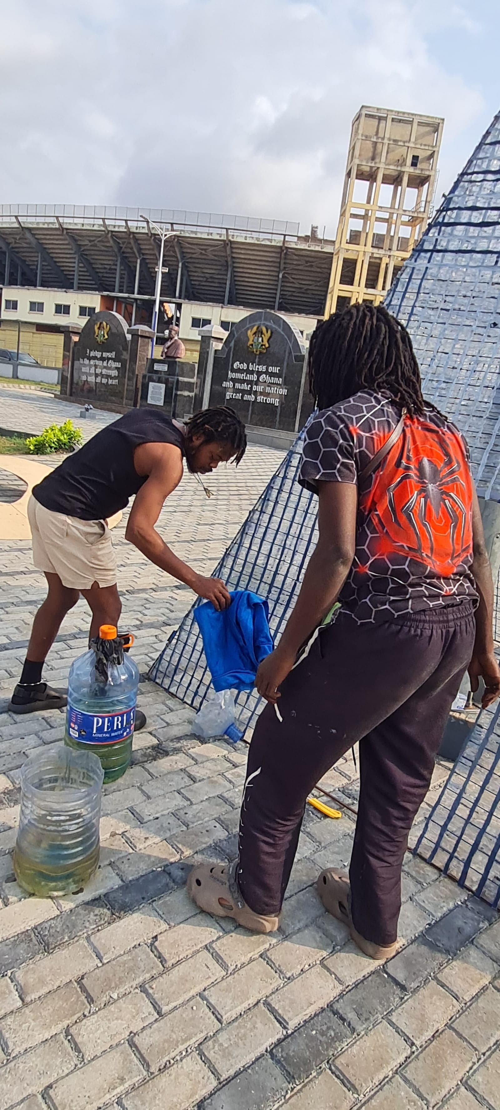Hands packing salvaged plastic into a cut bottle at the foot of a bottle-and-mesh tower